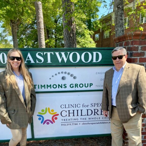 Brittany on the left and Paul on the right wearing a plaid blazer, blue button down, khakis, and black sunglasses.