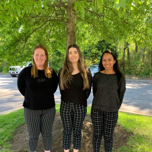 Three women wearing black sweaters and plaid black pants.