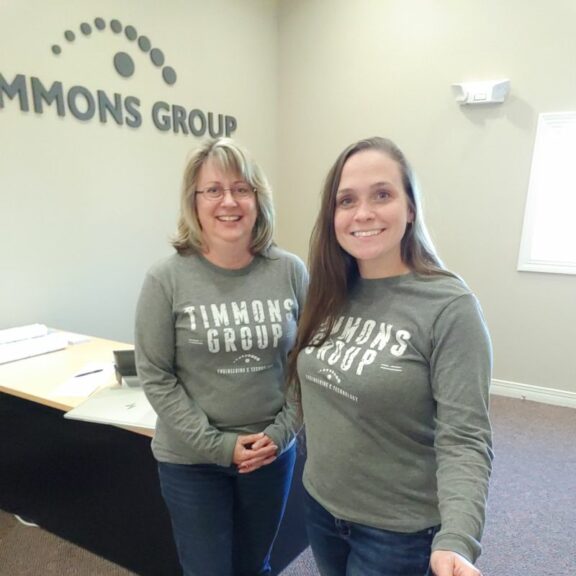 Two women wearing matching gray long-sleeved Timmons Group shirts. 