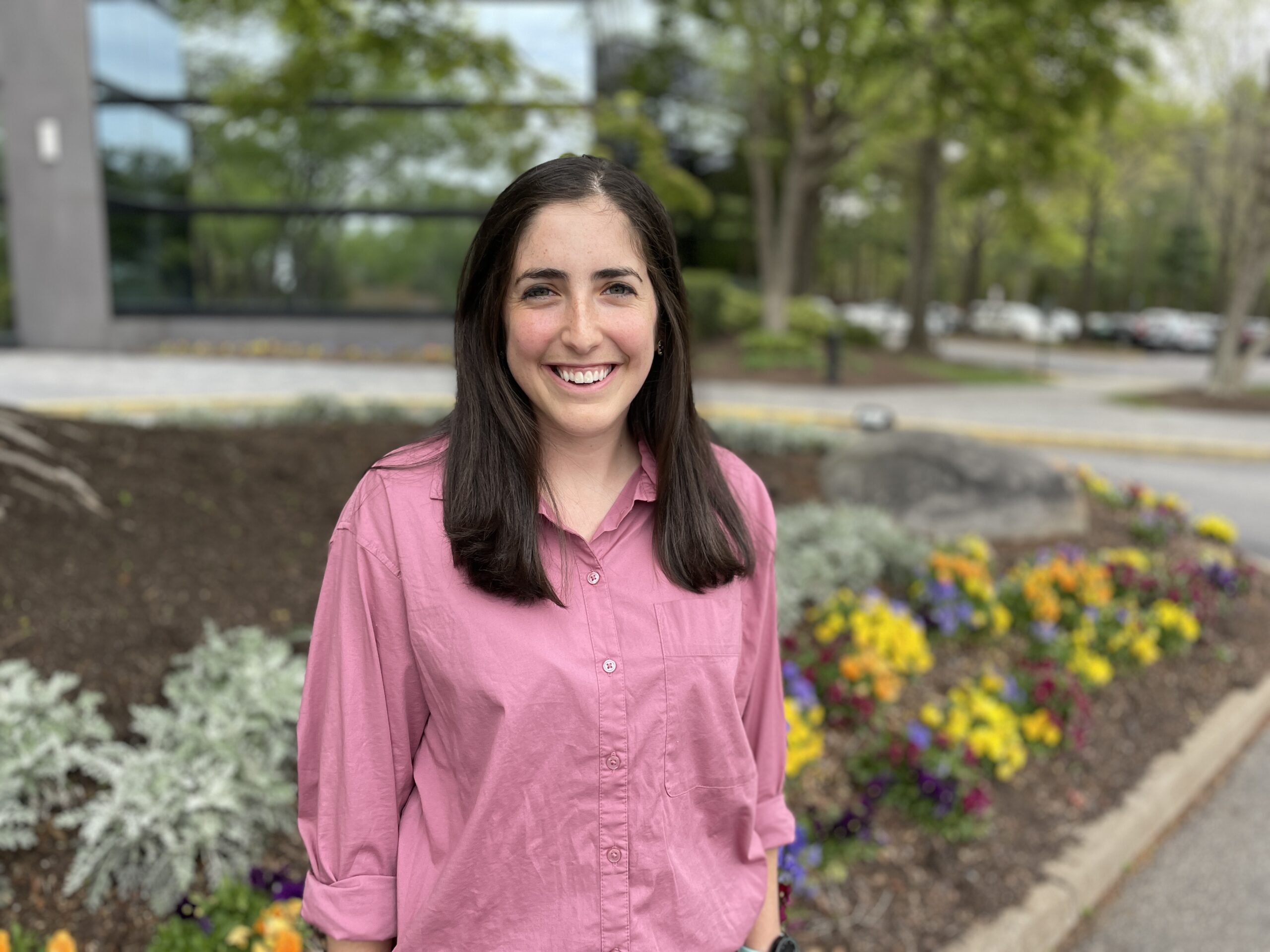 Leandra Colella smiling for picture while wearing pink button down shirt.