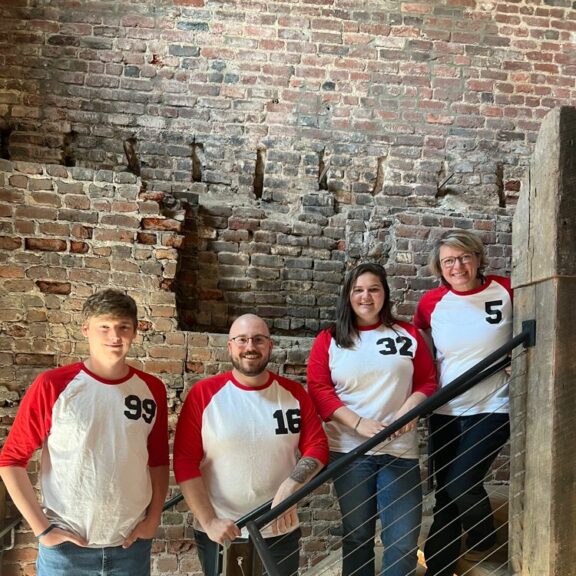 Two women and two men are wearing red and white baseball-esque shirts.