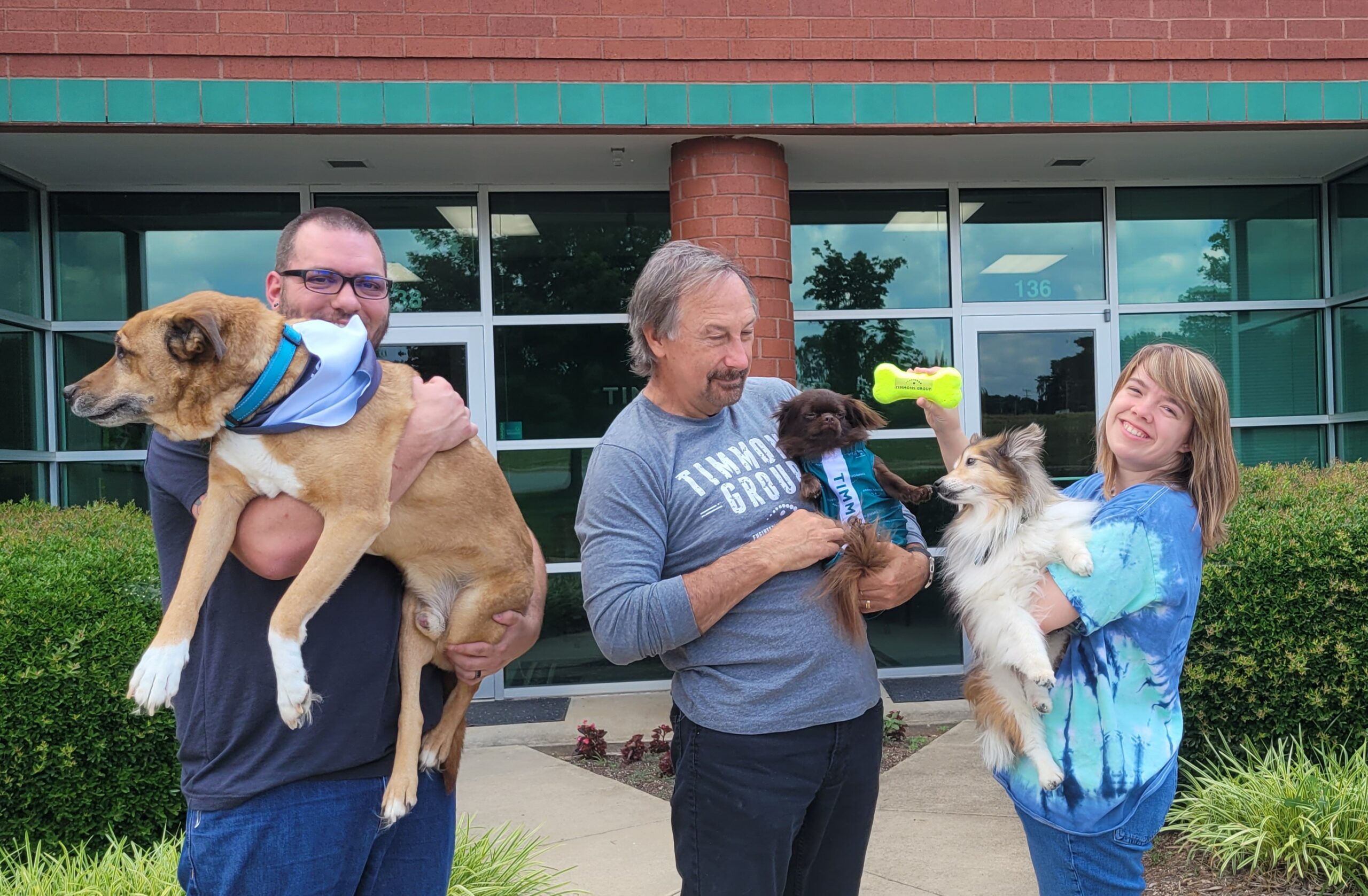 Three of our Greensboro office team members posing with their dogs outside of the office