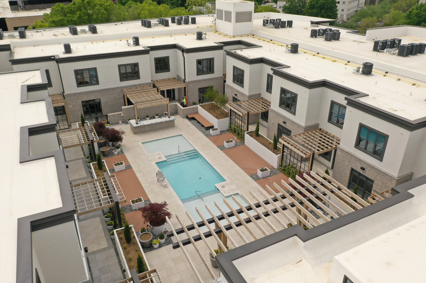 A photo of the pool oasis. The outside pool is located in the middle of the property. The brick surrounding the pool is a beige color. The outside brick is a clay color. The pool is decorated with many different plants.