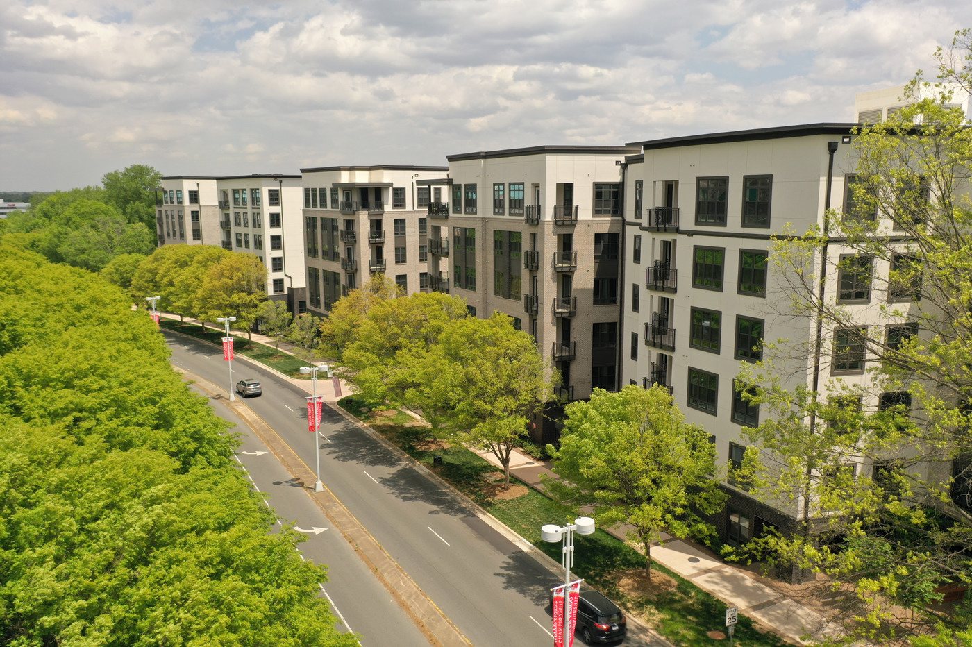 Another photo featuring the apartment's exterior. There's a sidewalk with many bright green trees decorating the median. Very beautiful place to take a stroll or run.