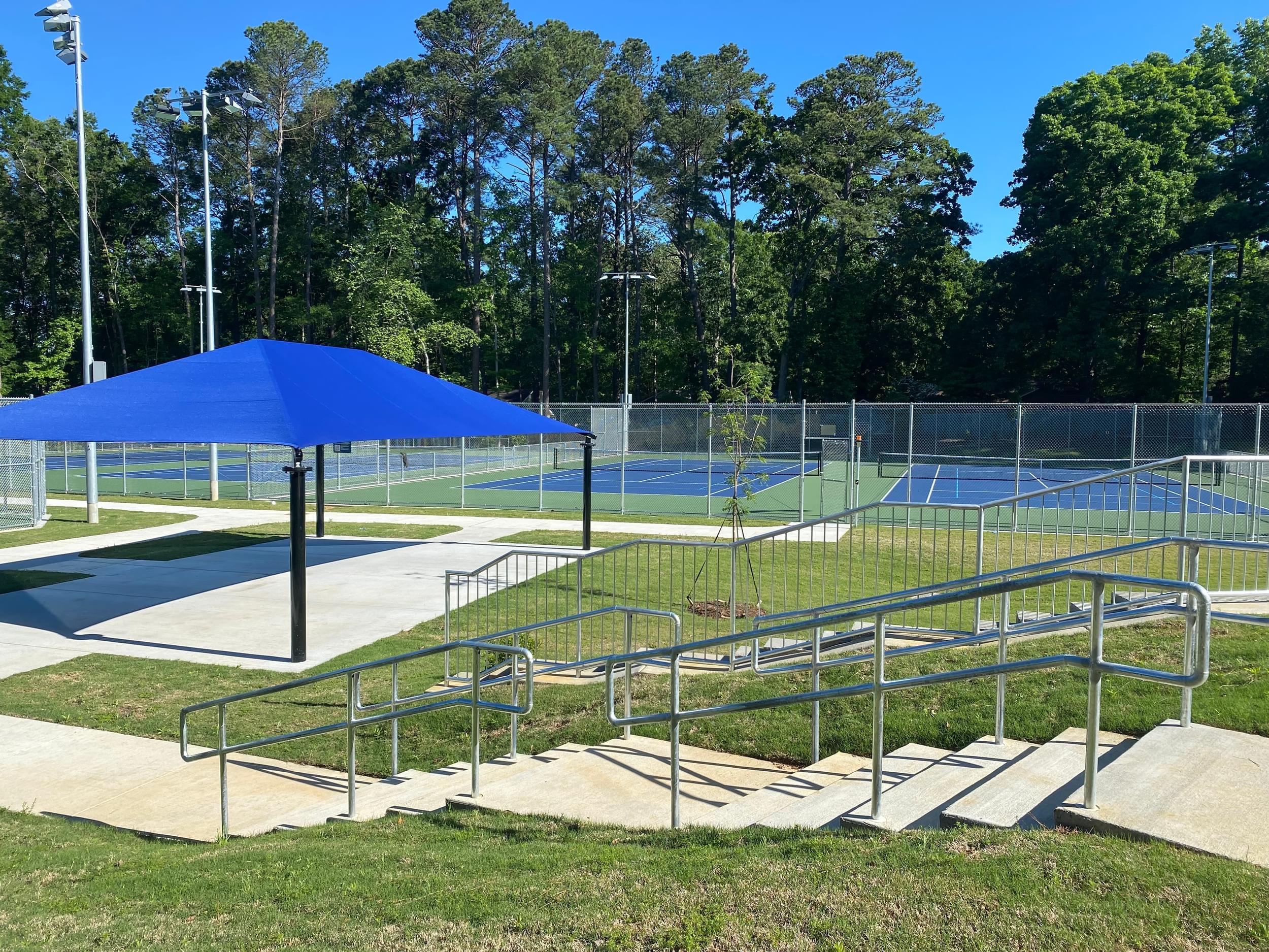 Picture of R.S. Dunham Park Courts featuring a cement staircase with metal railing and picnic shelter with a bright blue tent.