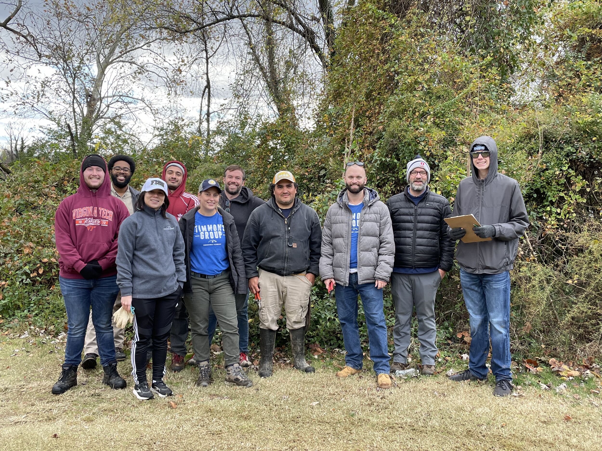 Ten Timmons Group employees standing in a horizontal line smiling for the picture. Behind them is green vegetation commonly found near streams and rivers.