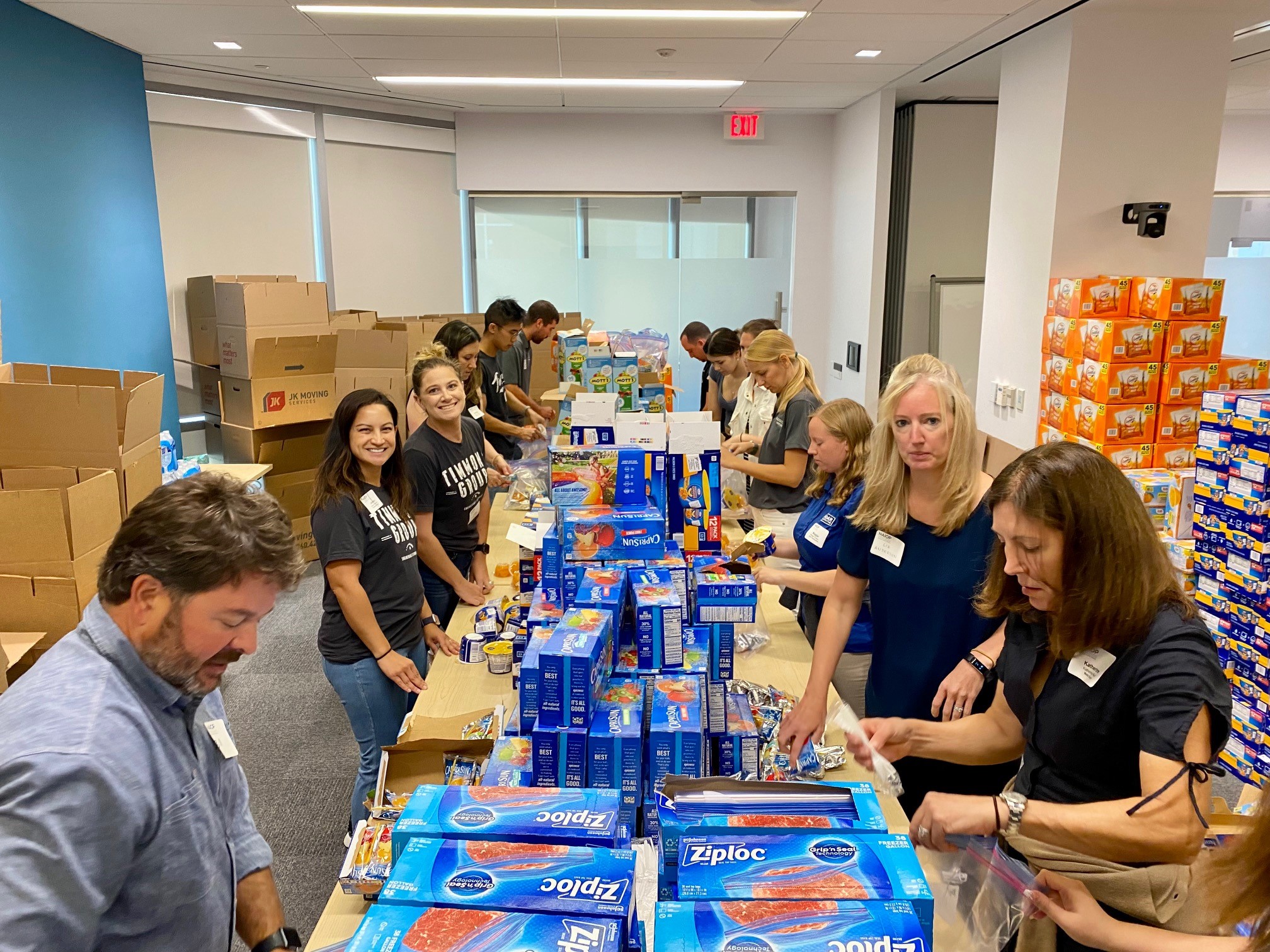 Timmons Group employees standing around a long table with boxes of ziplock bags and snacks in front of them.