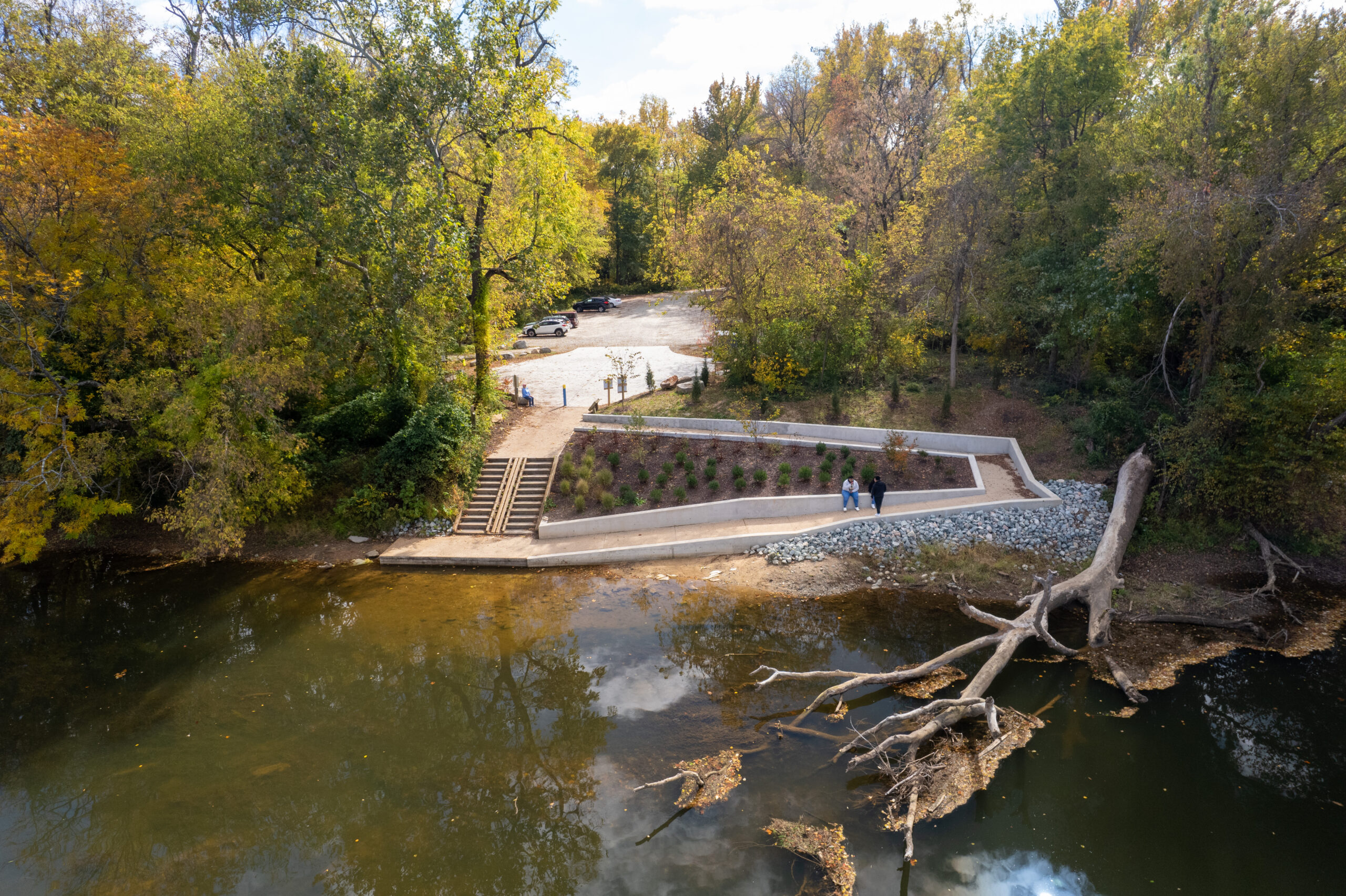 Aerial photo of the universal access ramp. there is a stair case on the left side of the ramp that has direct access from the parking lot to the launch point. People are outside enjoying the ramp and the calm water.