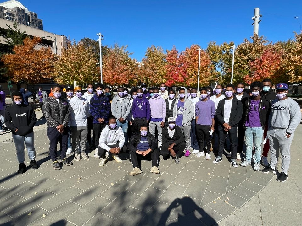 Jalen with a large group of men all wearing a matching color scheme of purple, black, and gray. Everyone in the photo is wearing a purple mask.