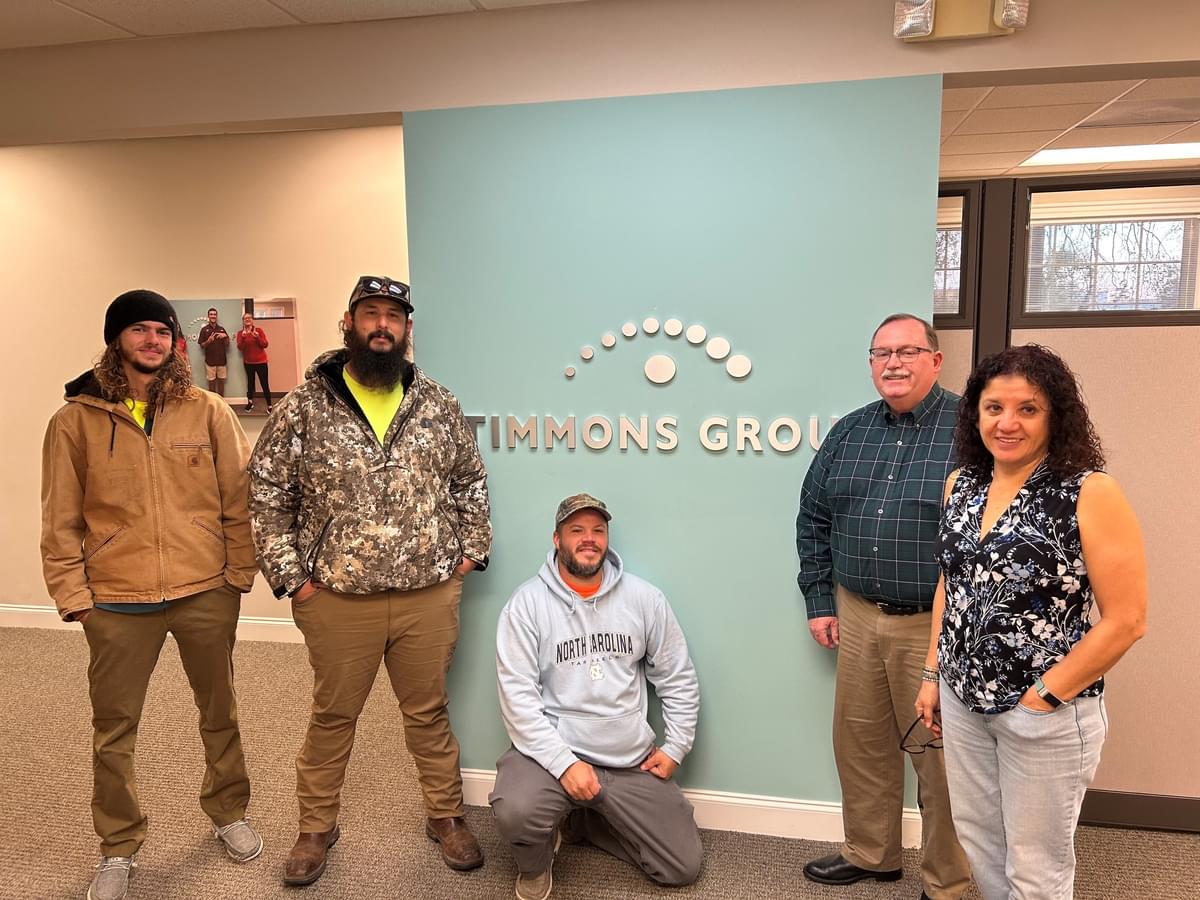 Ed Jordal and his four team members pose together for a group photo in front of a baby blue wall with a silver Timmons Group logo on it.