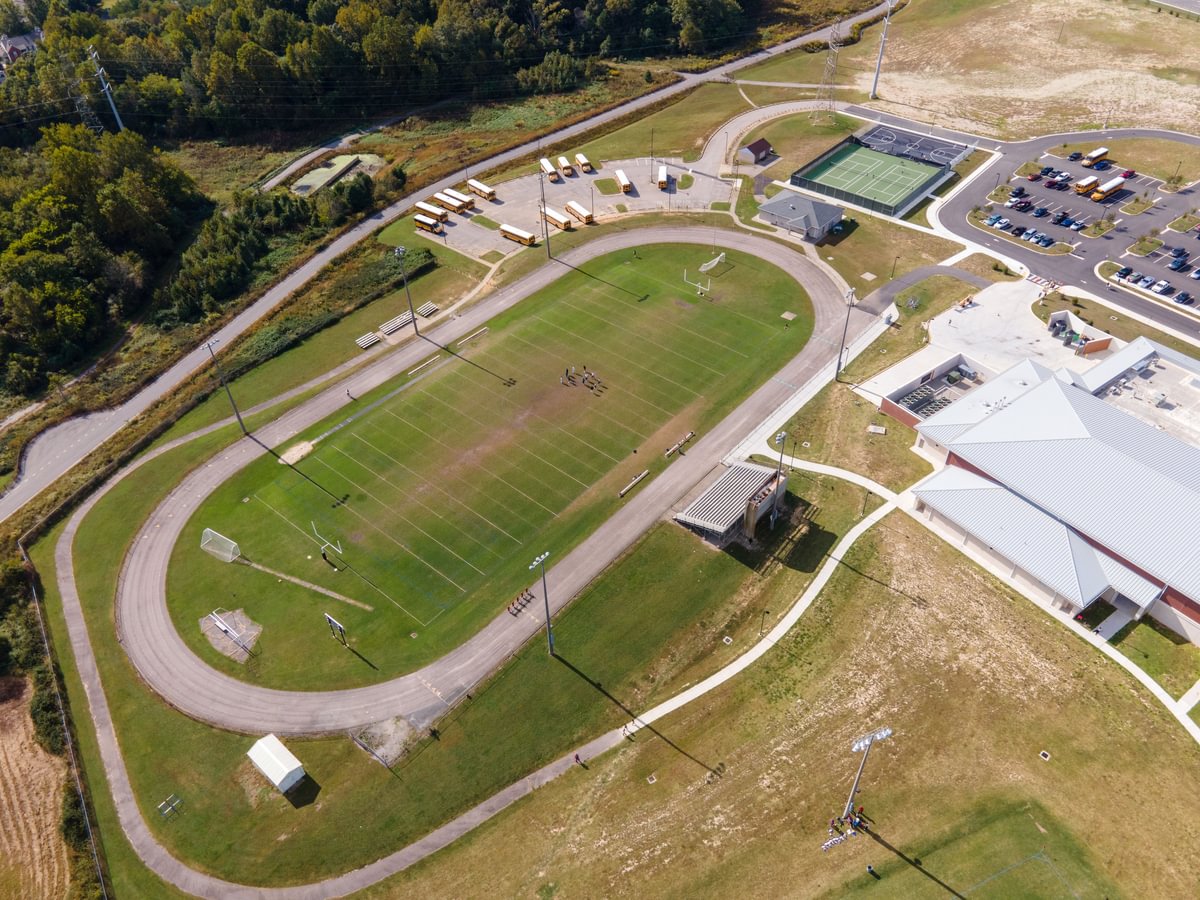 Above aerial photo of the Manchester Middle School football field with wrap around track, a smaller bus loop, tennis court, and basketball court.