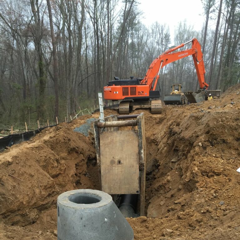 A construction site featuring a large excavation hole in the ground, surrounded by machinery and safety barriers.