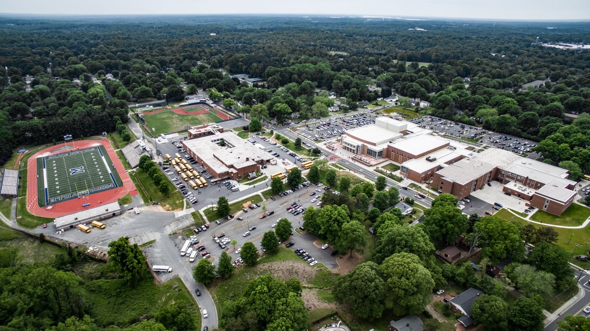 Aerial view of Mooresville High School in Mooresville, North Carolina featuring the football field with a giant blue M painted in the middle, the school campus, parking lots, adn teh baseball field.