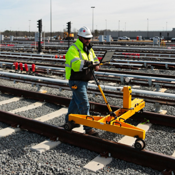 A man stands on a train track, surveying the area with rail survey equipment.